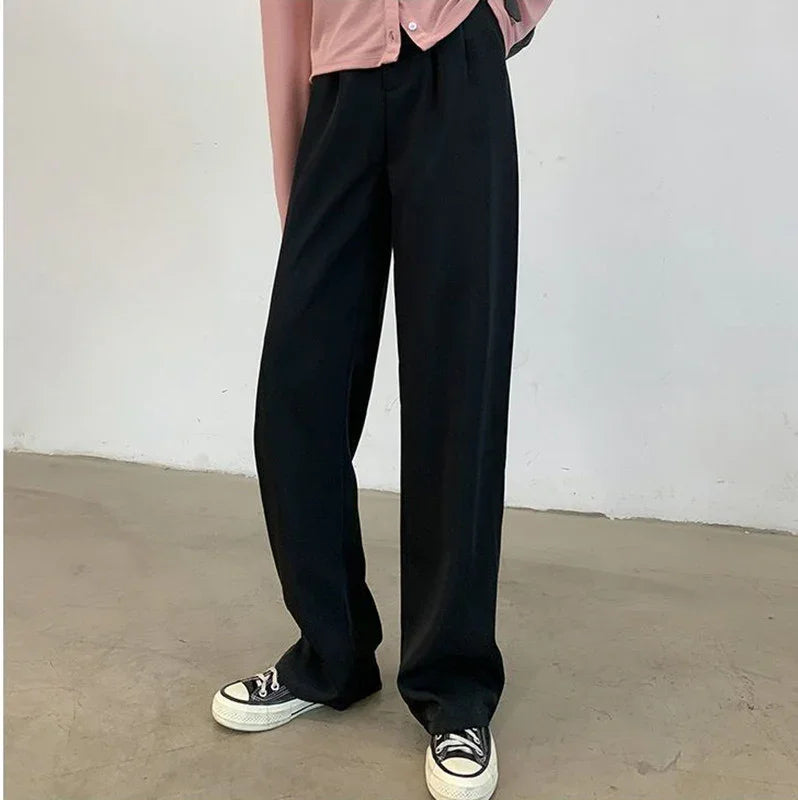 Person wearing black wide-leg trousers and black low-top sneakers on concrete floor