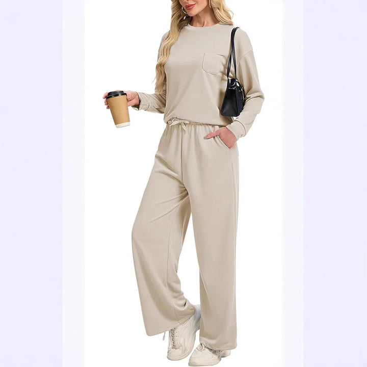 Woman wearing beige long-sleeve top and matching wide-leg pants holding coffee cup, black shoulder bag, white sneakers