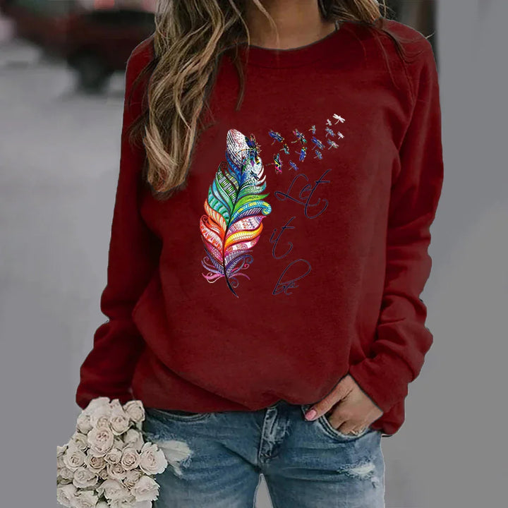 Woman wearing red sweatshirt with colorful feather and dragonfly design and text Let it be