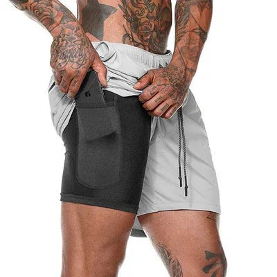 Man wearing gray shorts with built-in black pocket holding a phone, showcasing tattooed arms and legs