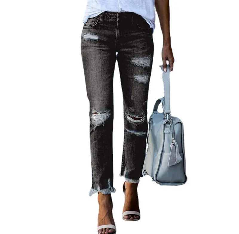 Woman wearing distressed black jeans with frayed hems and white sandals, holding light gray handbag