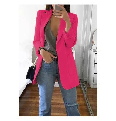 Woman wearing bright pink blazer, gray deep V-neck top, and blue jeans taking mirror selfie indoors