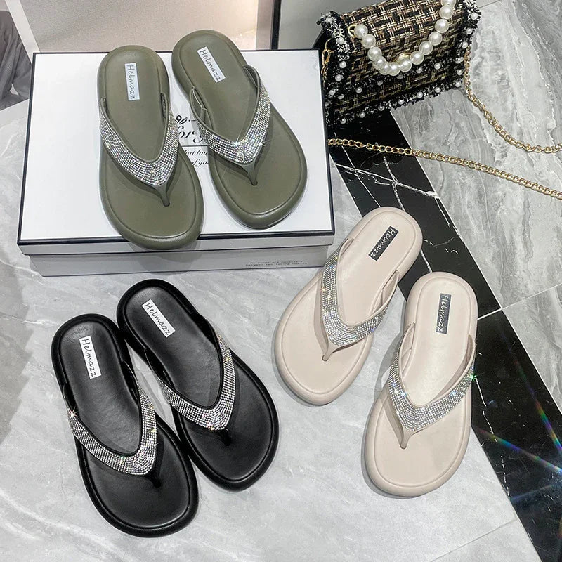 Three pairs of glittery rhinestone flip-flops in olive green, black, and beige on marble floor with a tweed handbag