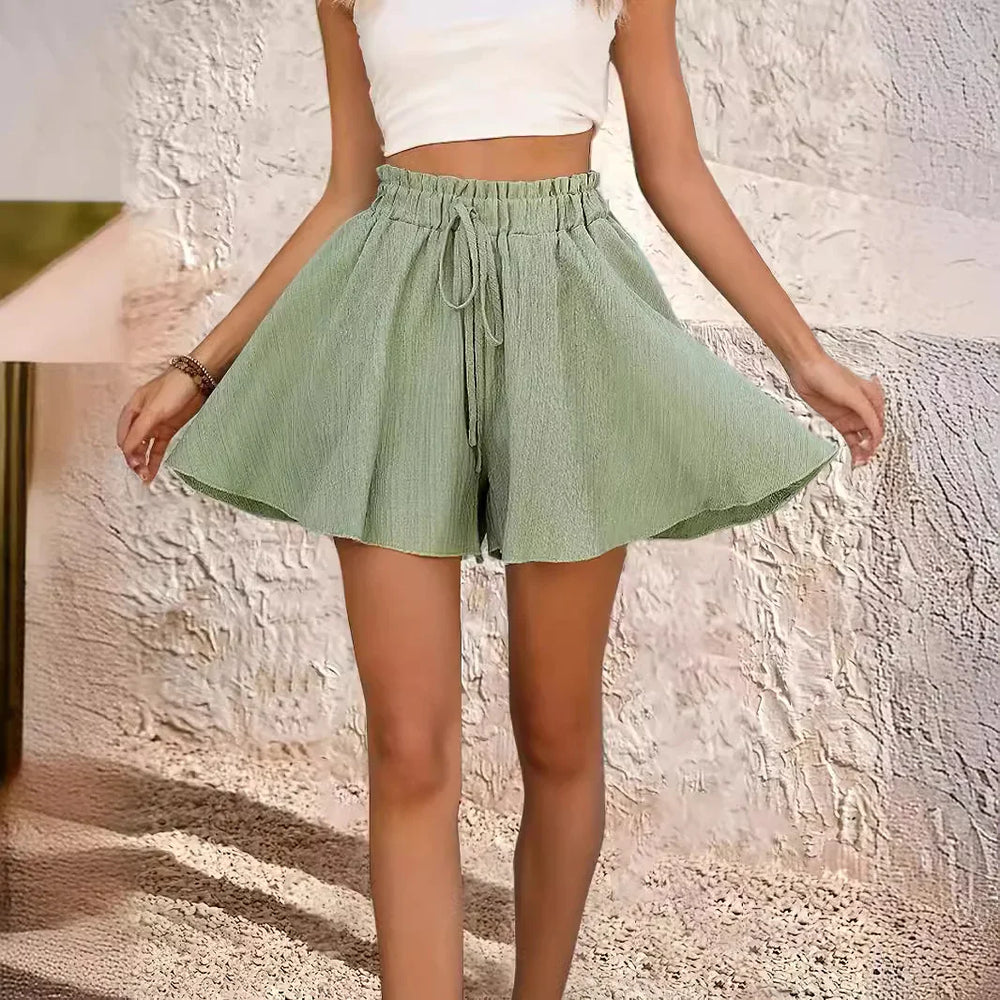 Woman wearing light green high-waisted drawstring shorts and white crop top in textured room