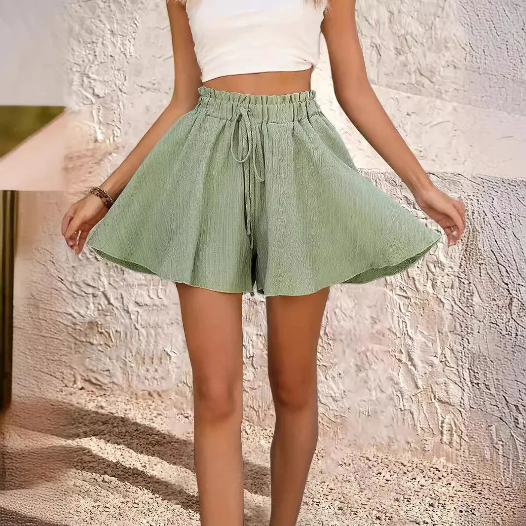 Woman wearing light green high-waisted drawstring shorts and white crop top in textured room