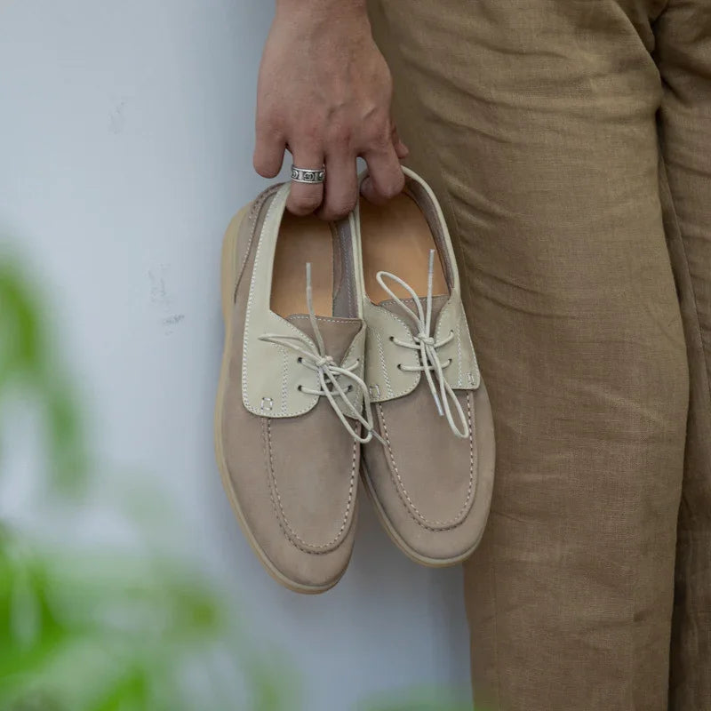 Hand holding beige and cream leather casual shoes against a person wearing brown pants