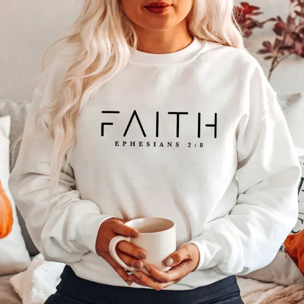 Woman wearing white sweatshirt with FAITH EPHESIANS 2:8 text holding white mug indoors