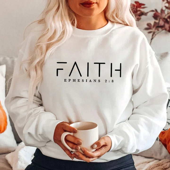Woman wearing white sweatshirt with FAITH EPHESIANS 2:8 text holding white mug indoors