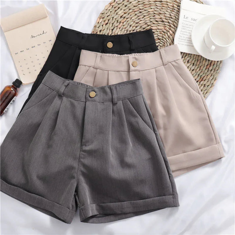 Three pairs of pleated high-waisted shorts in black, beige, and gray with button detail on white background