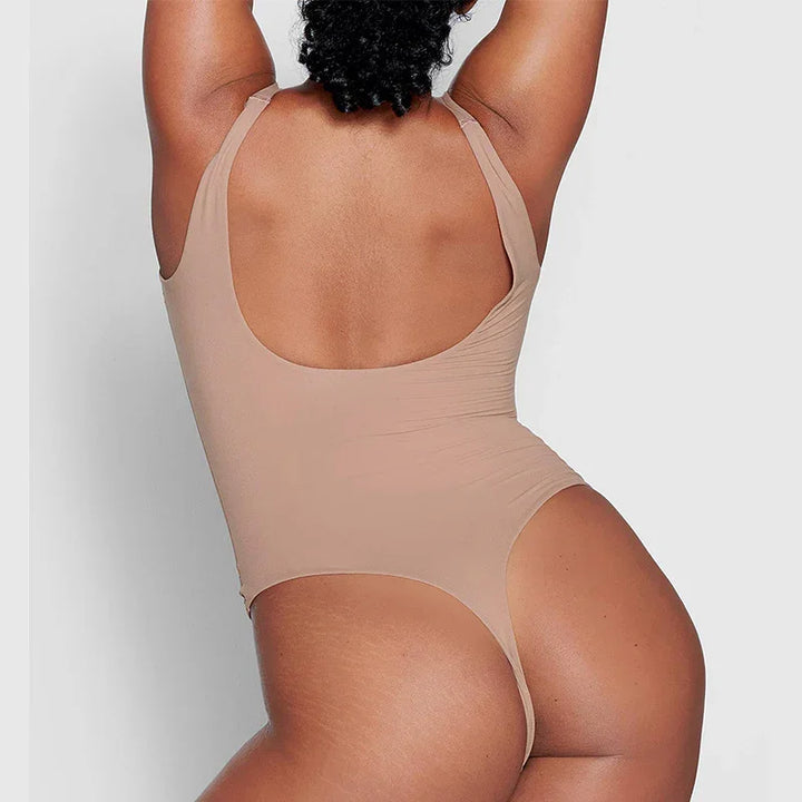 Back view of woman wearing beige high-cut bodysuit with scoop back against gray background