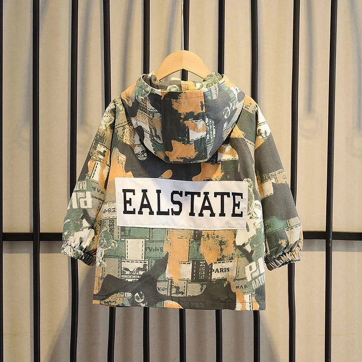 Kids hooded jacket with abstract camo print and EALSTATE text on back, hanging on wooden hanger