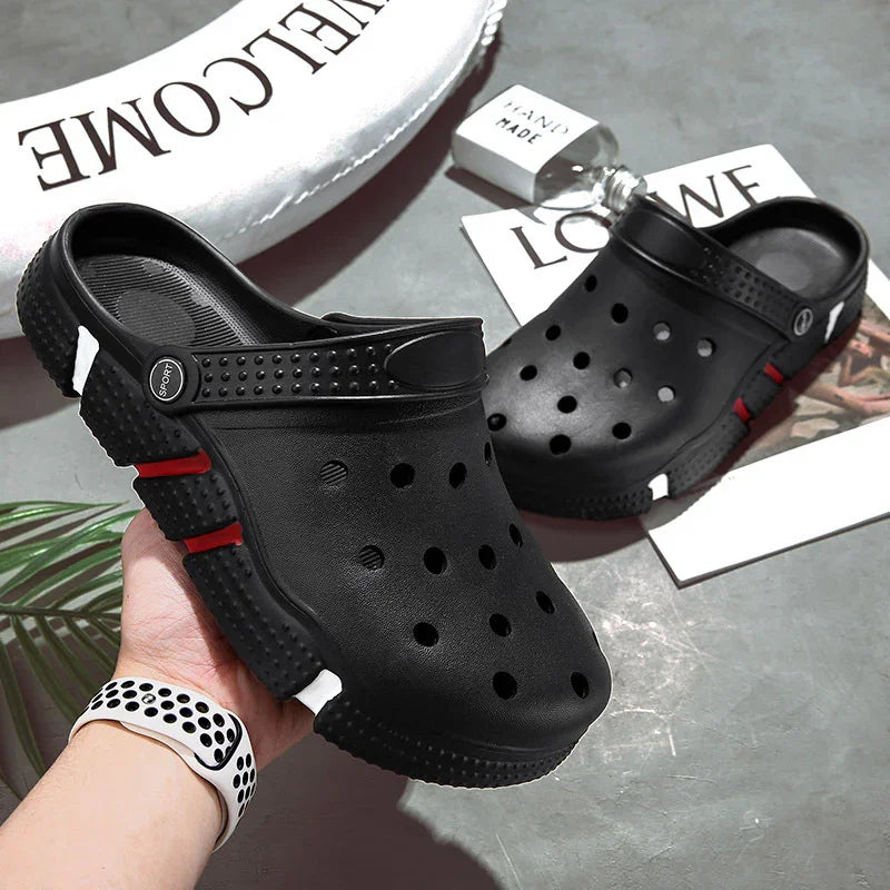 Black slip-on clogs with ventilation holes and red and white sole accents on gray surface