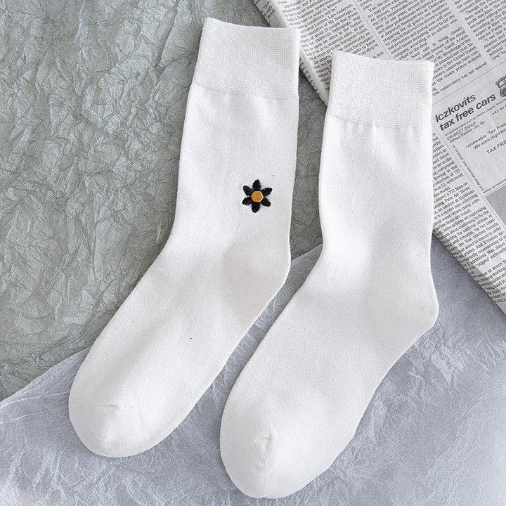 Pair of white crew socks with one sock featuring a small black flower with orange center embroidered