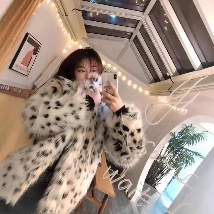 woman taking mirror selfie wearing white and black spotted faux fur coat in cozy room with string lights