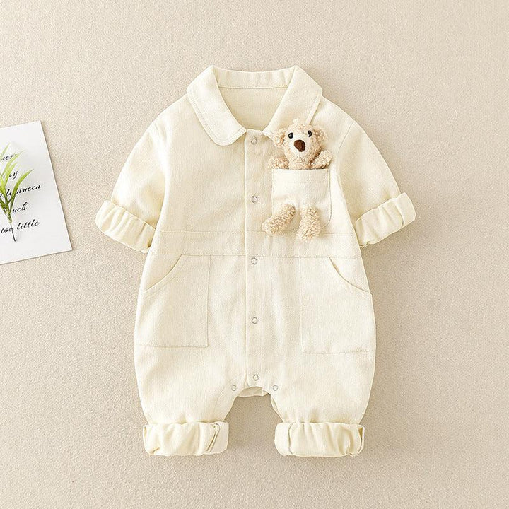 Cream-colored baby romper with rolled sleeves and legs, featuring front pockets and a plush teddy bear in chest pocket
