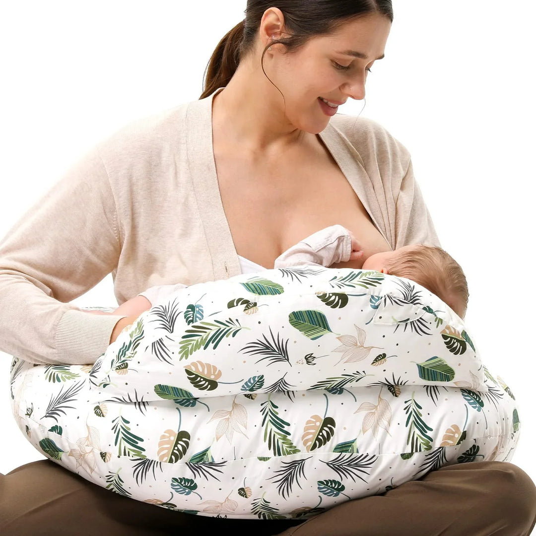Mother breastfeeding baby using a white nursing pillow with green and beige leaf pattern
