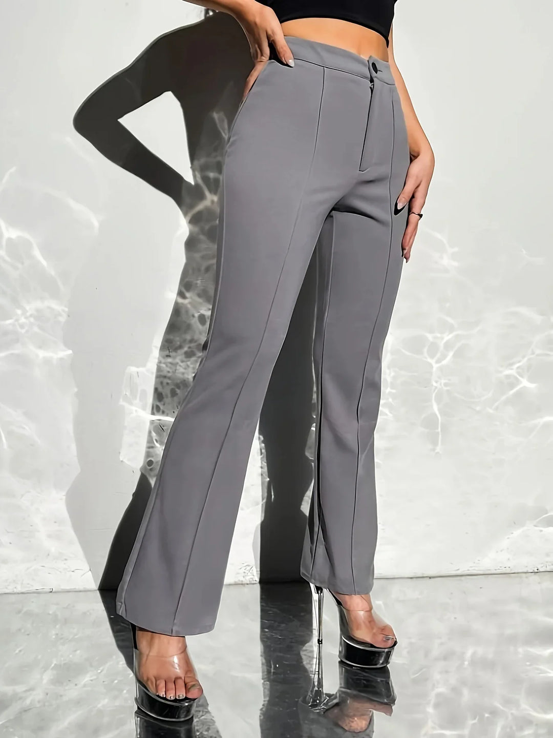 Woman wearing grey flare pants and clear platform heels standing against white wall with light reflections