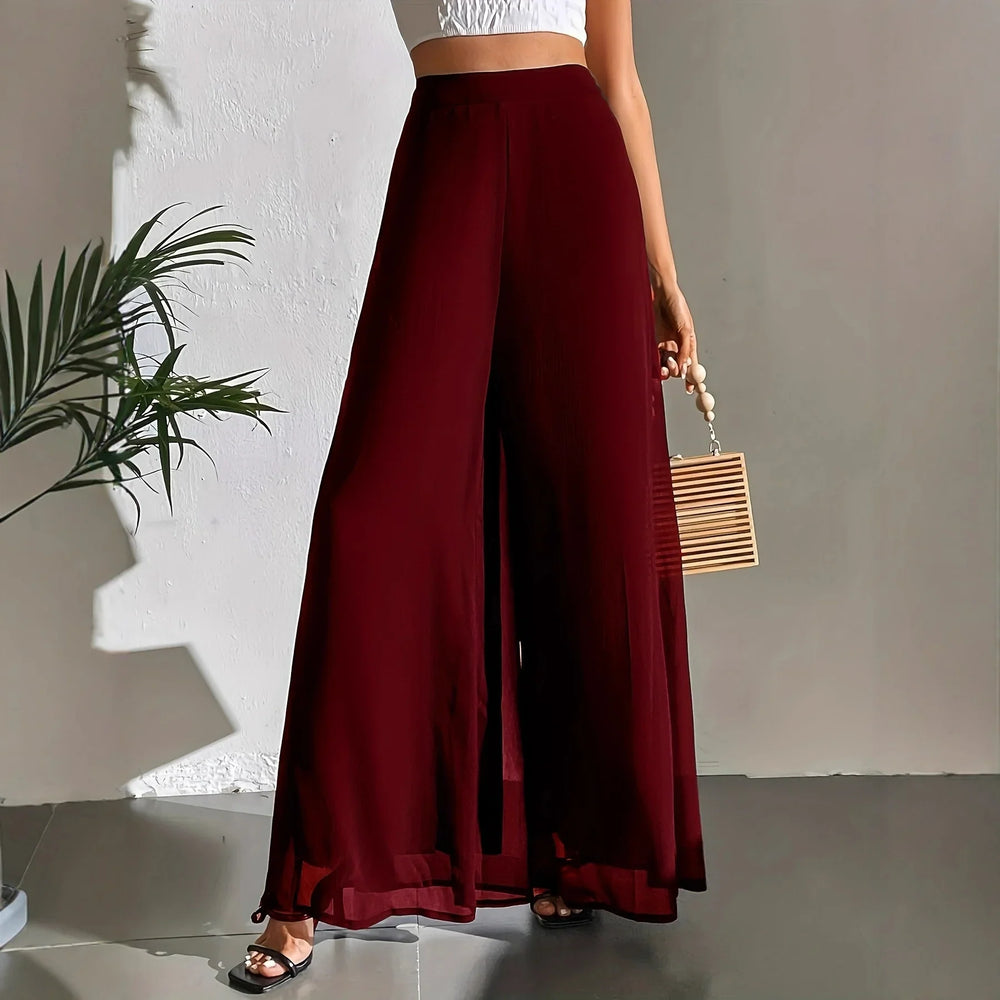 Woman wearing high-waist wide-leg burgundy pants with a white crop top and black heels indoors