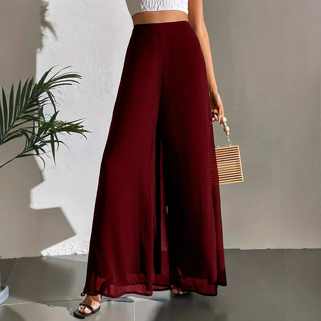 Woman wearing high-waist wide-leg burgundy pants with a white crop top and black heels indoors