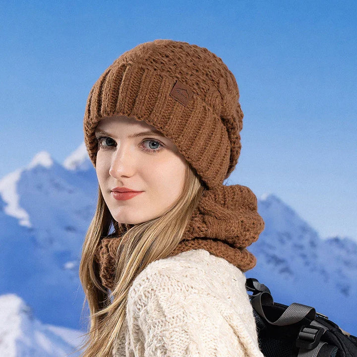 Young woman wearing brown knit beanie and scarf with white sweater, snowy mountain background
