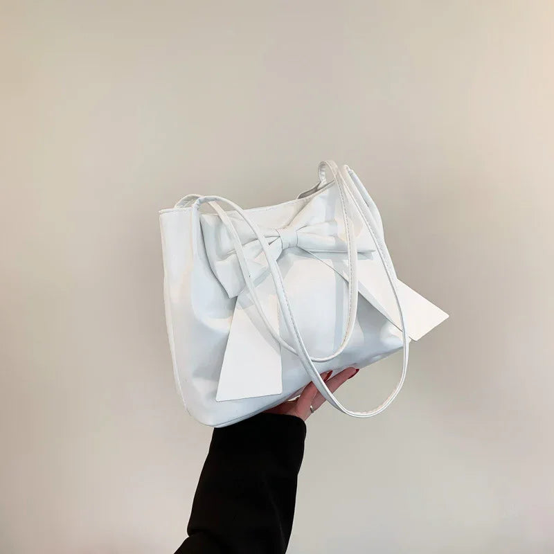 White leather handbag with a large bow detail, held by a hand against a plain background