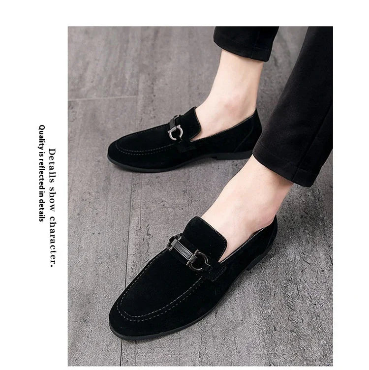 Black suede loafers with silver metal buckle on men's feet wearing black pants on gray floor