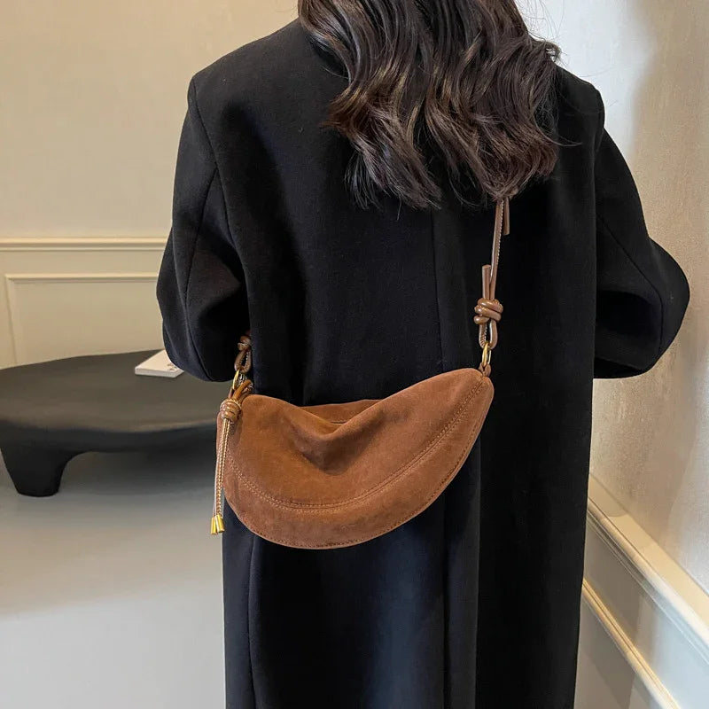 Woman wearing black coat with brown suede crescent shoulder bag in minimalist room