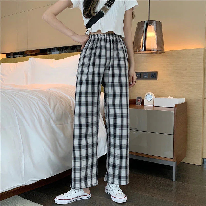Woman wearing high-waist black and white plaid wide-leg pants and white sneakers in modern bedroom