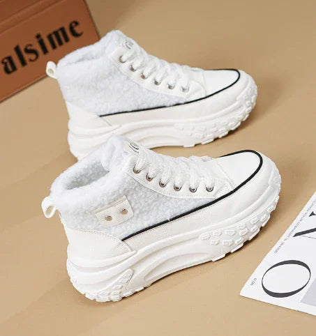 Pair of white high-top sneakers with fluffy interior and thick textured soles on beige surface