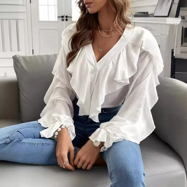 Woman wearing white ruffled blouse and blue jeans sitting on gray couch in modern room
