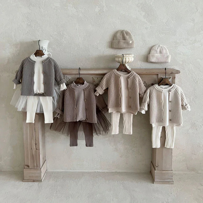 Neutral-toned toddler outfits with knit cardigans, leggings, tulle skirts, and knit beanies displayed on wooden hangers