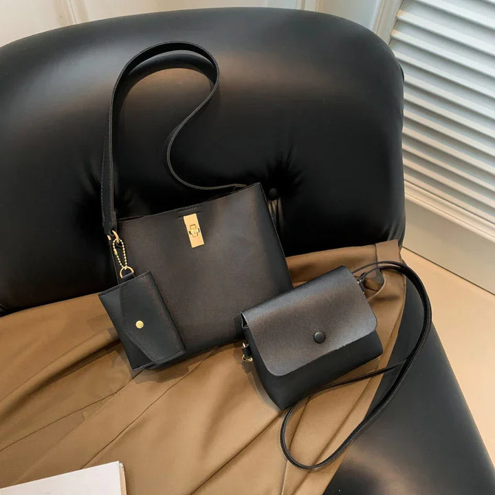 Black leather bucket bag with gold clasp, small flap crossbody bag, and matching cardholder on black couch