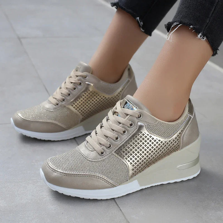 Women's metallic gold wedge sneakers with mesh and perforated details on gray floor