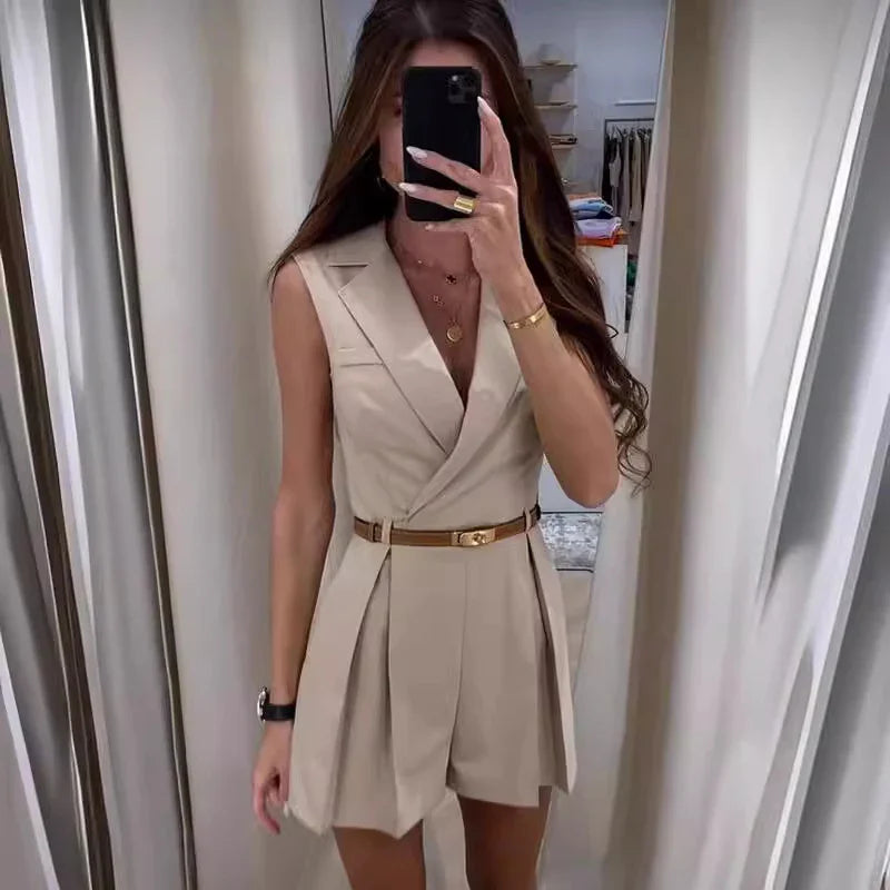 Woman taking mirror selfie wearing sleeveless beige blazer dress with brown belt and gold jewelry