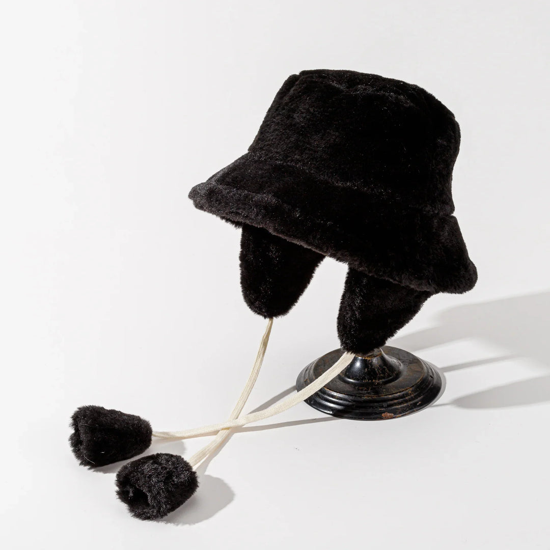 Black faux fur trapper hat with ear flaps and cream ties on black stand