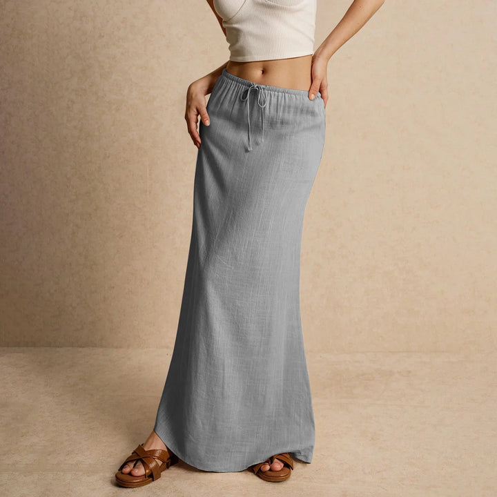 Woman wearing a light gray drawstring maxi skirt and brown sandals on beige background