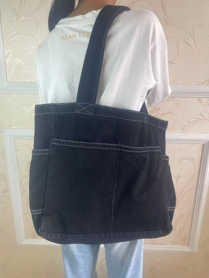 Person wearing white shirt and blue jeans carrying large black canvas tote bag with white stitching
