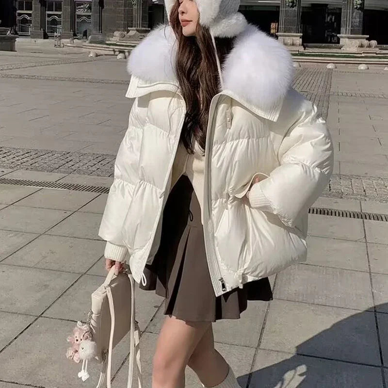 Woman wearing white puffer jacket with fur collar and earmuffs, brown skirt, holding beige bag outdoors