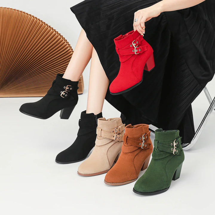 Woman wearing black heeled ankle boots and holding red boots with five pairs of ankle boots in black, beige, brown, green, and red on white floor