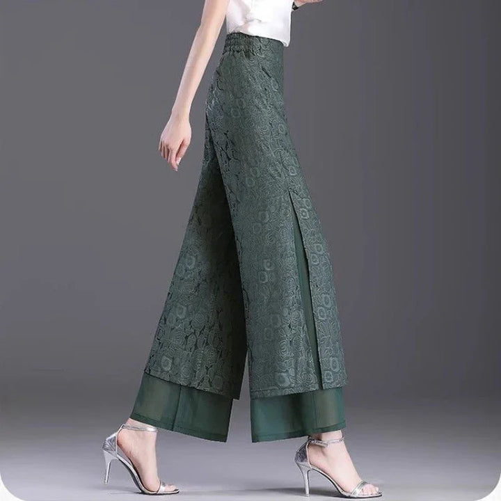 Woman wearing dark green lace wide-leg pants with side slits and sheer underlayer, paired with silver heels
