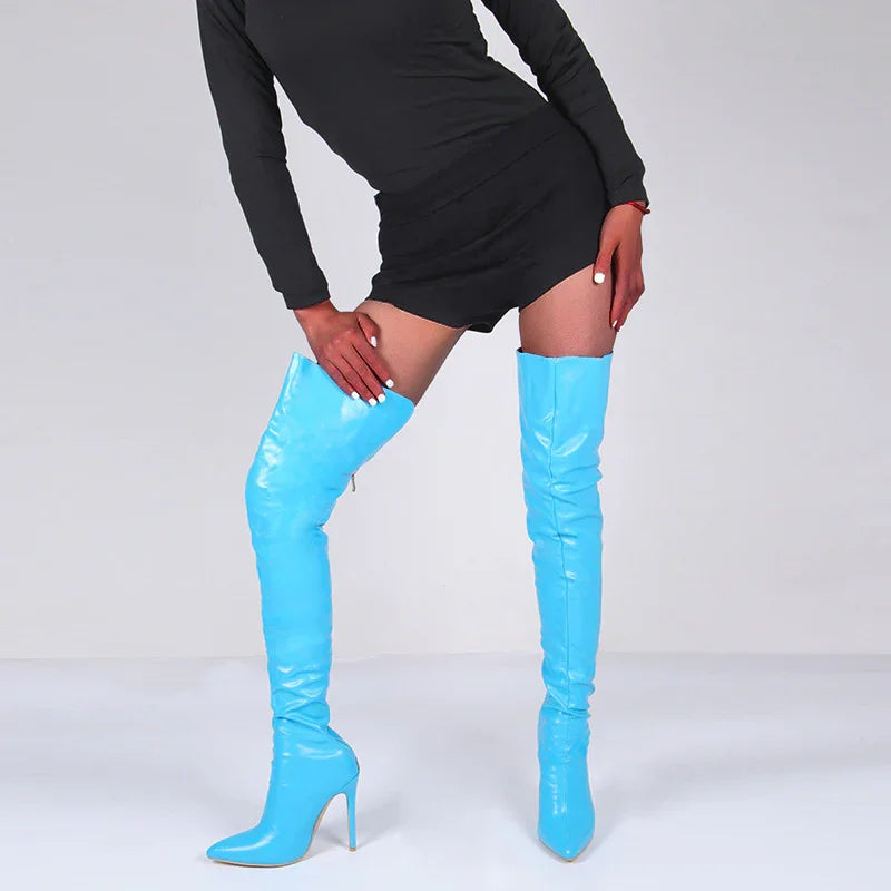 Woman wearing shiny blue thigh-high stiletto boots and a black mini dress against white background