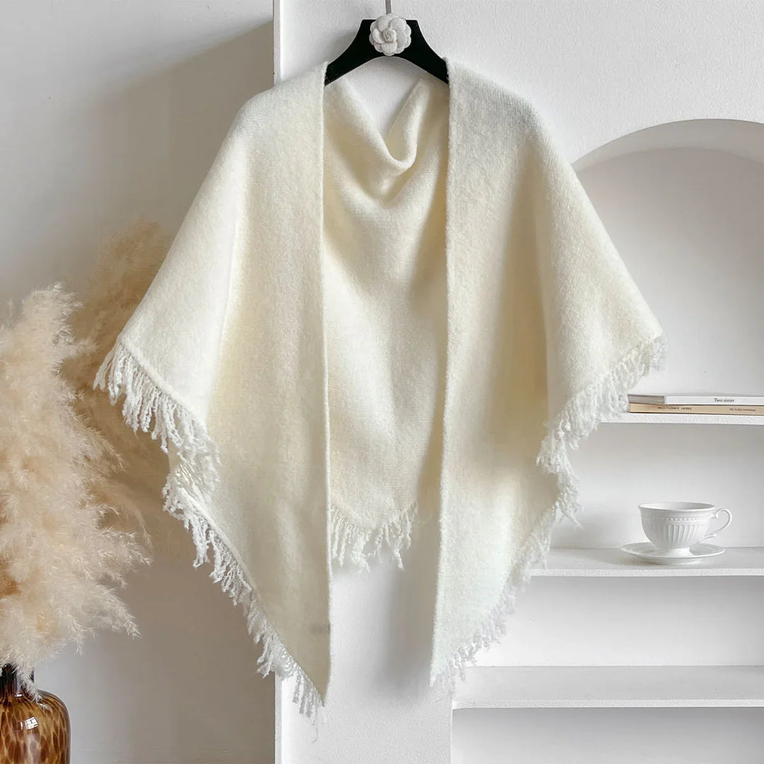 Soft white fringed shawl hanging on a black hanger against a white wall with pampas grass and shelves