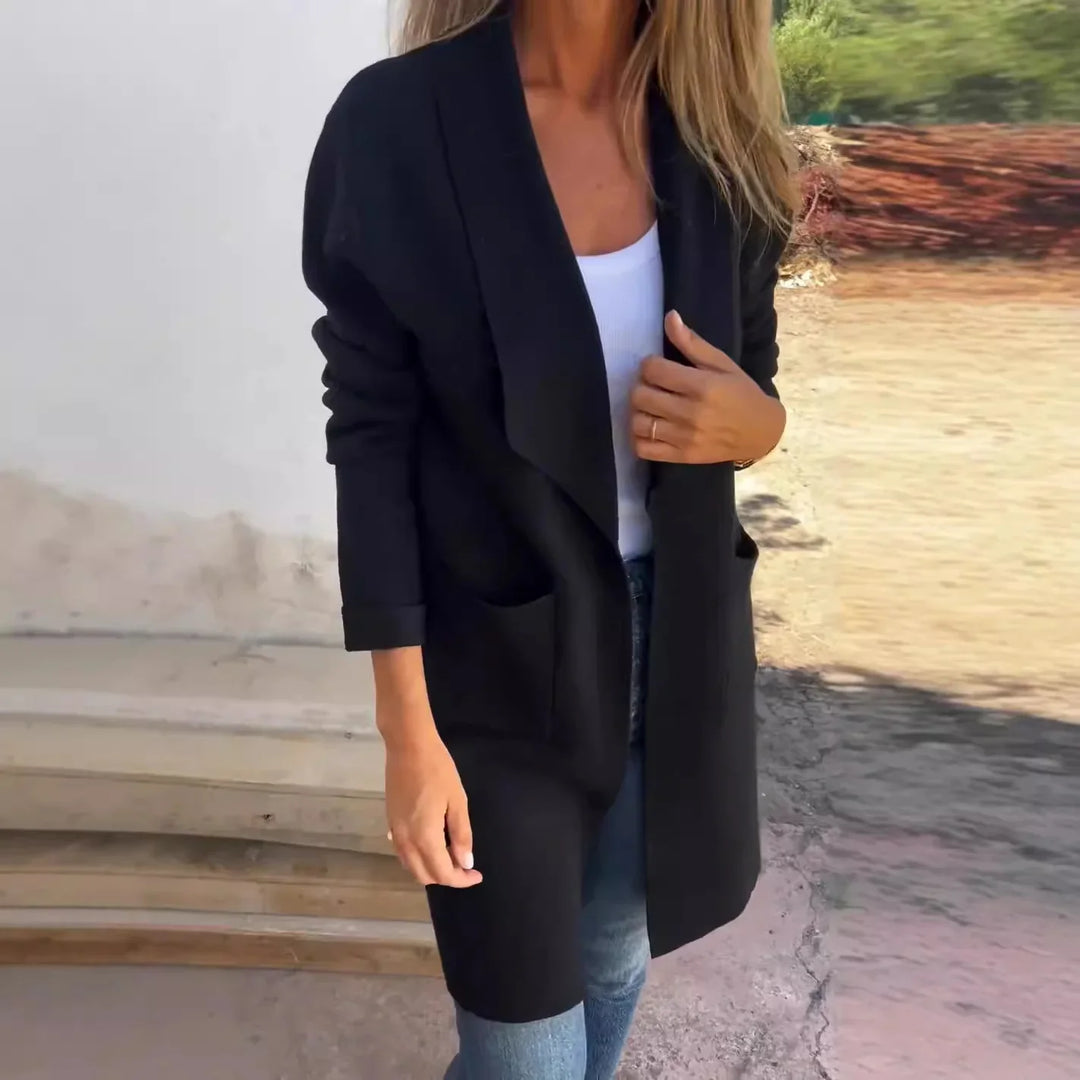 Woman wearing black open-front cardigan over white top and blue jeans outdoors