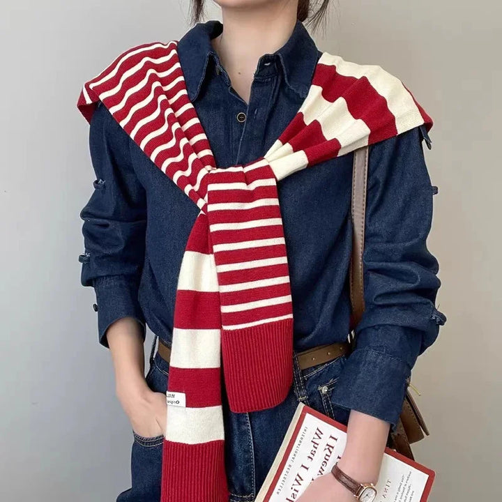 person wearing dark denim shirt with red and white striped scarf draped over shoulders holding book