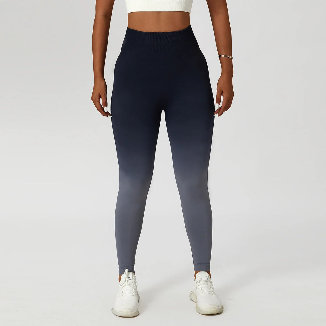 Woman wearing high-waisted ombre navy leggings, white crop top and sneakers against white background