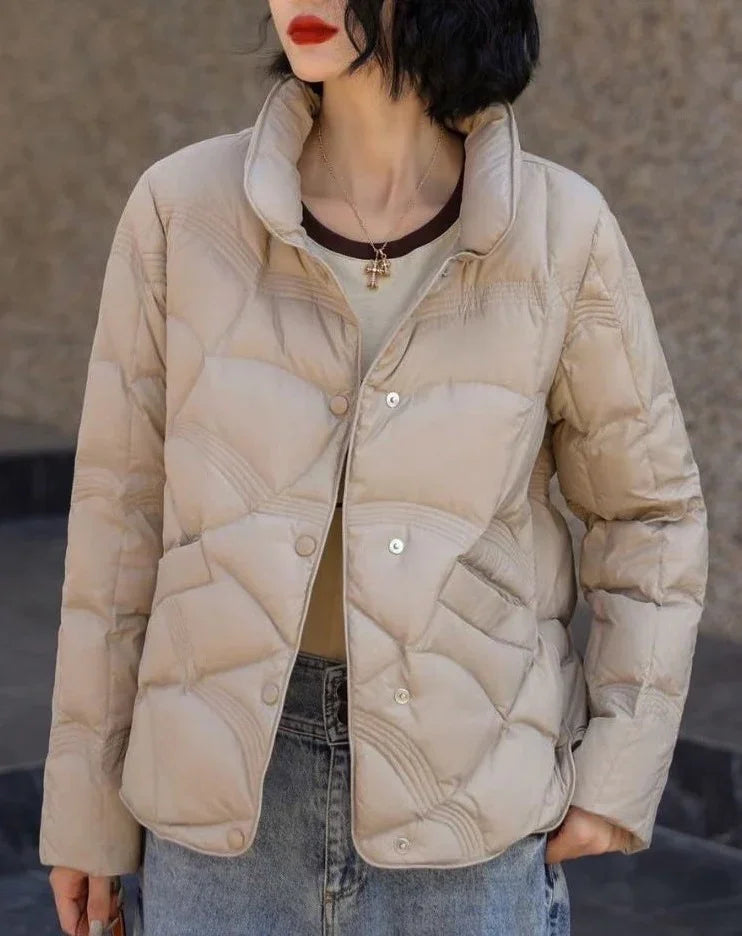 Woman wearing beige quilted puffer jacket with snap buttons, paired with blue jeans and red lipstick