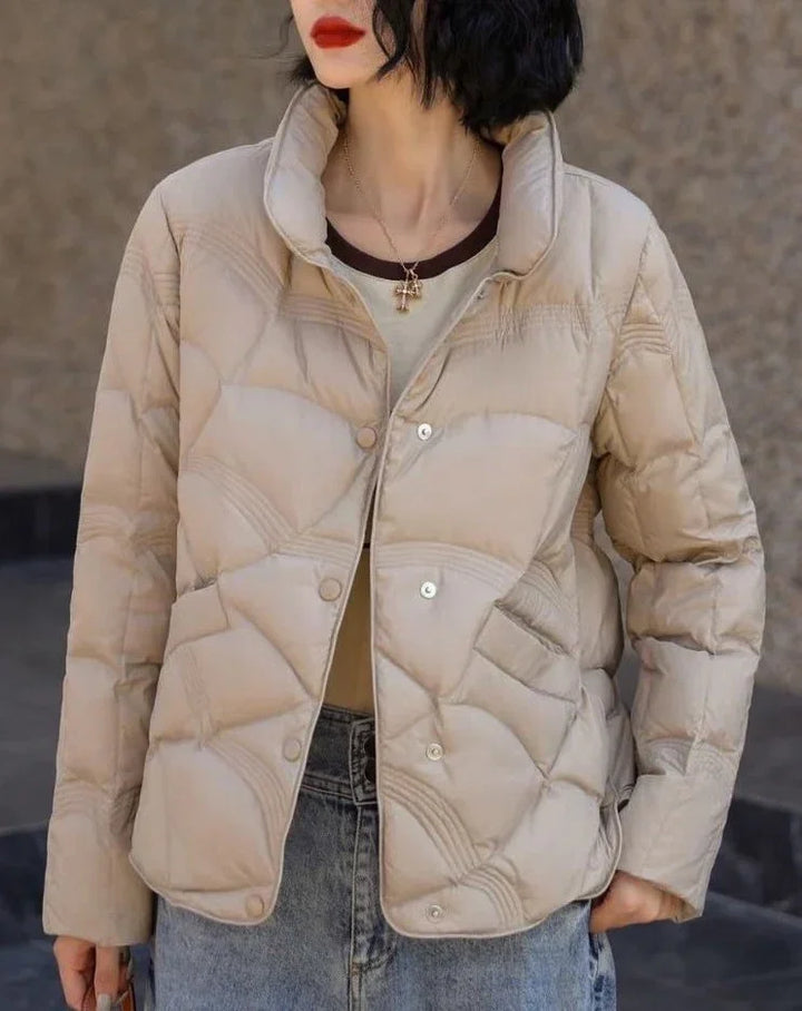 Woman wearing beige quilted puffer jacket with snap buttons, paired with blue jeans and red lipstick