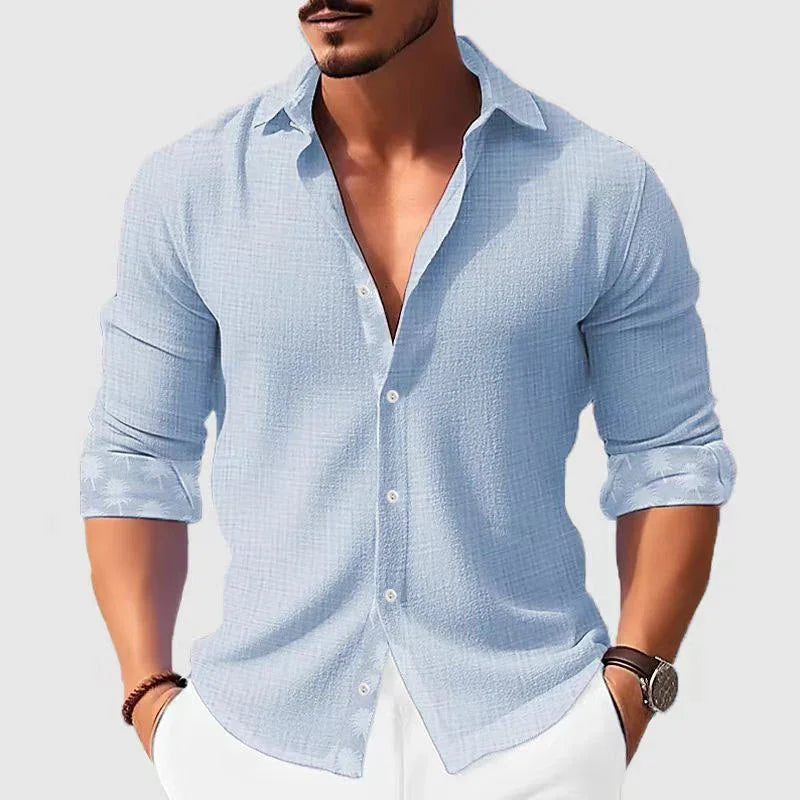 Man wearing light blue textured long sleeve button-down shirt with rolled cuffs and white pants