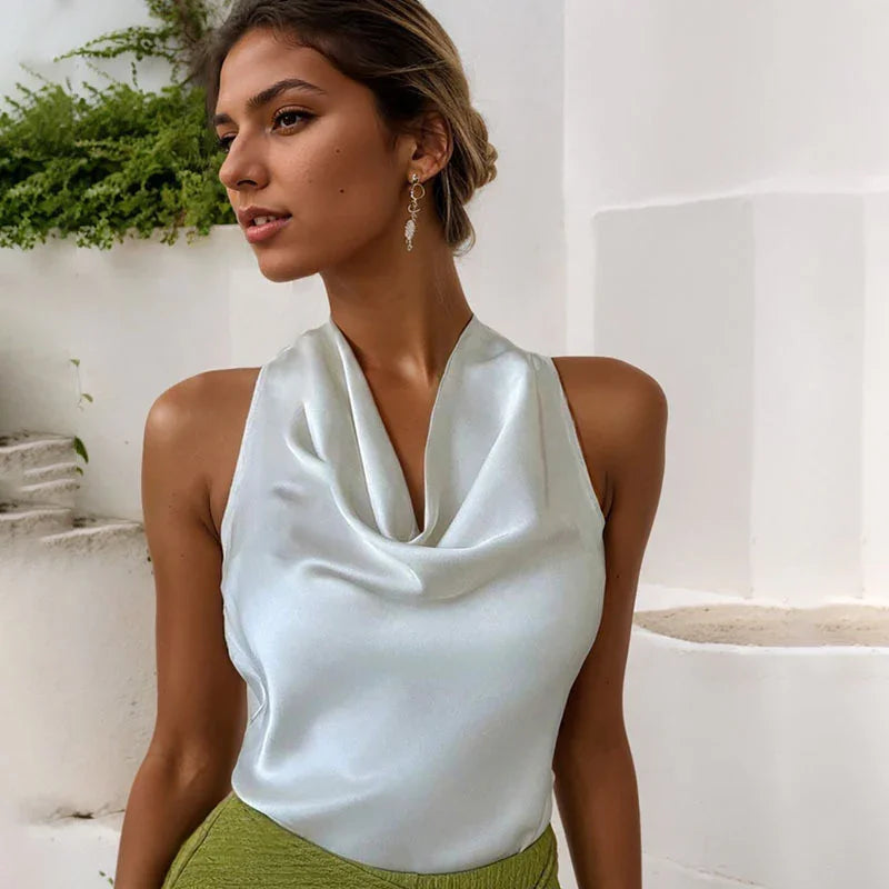 Woman wearing a white satin cowl neck top and olive green skirt with gold dangling earrings