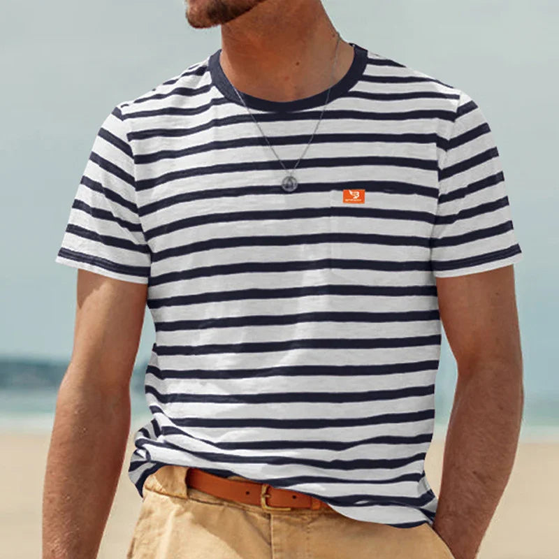 Man wearing navy and white striped t-shirt with small orange logo, tan belt, and beige pants at beach
